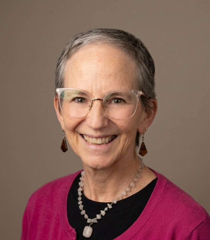A woman with short gray hair wearing glasses and smiling